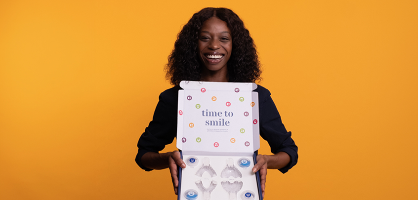 Woman holding a product box with 'time to smile' text against an orange background