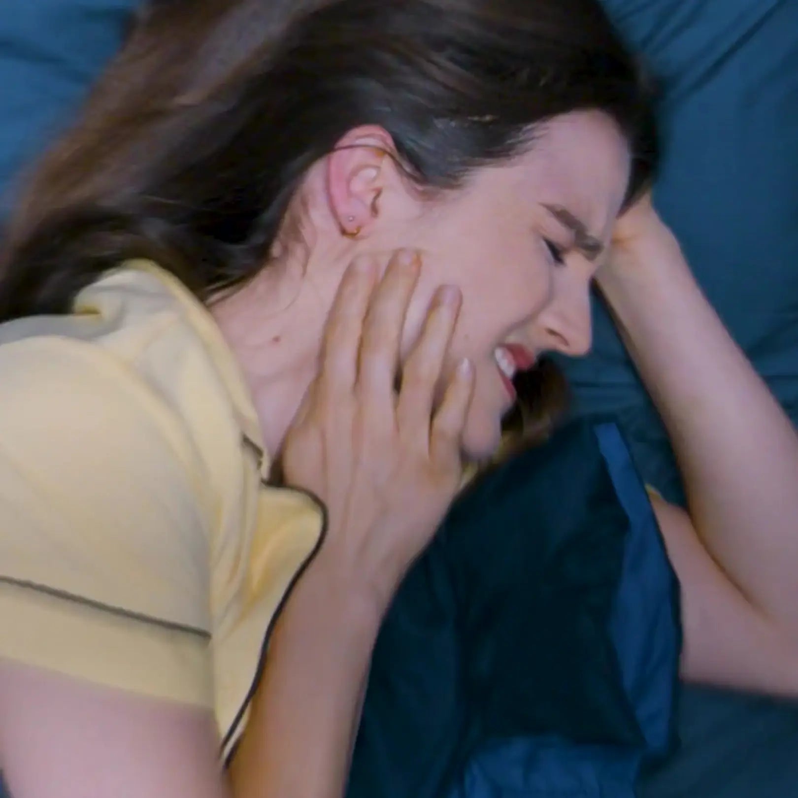 Woman in yellow shirt holding her head in distress on a blue couch.