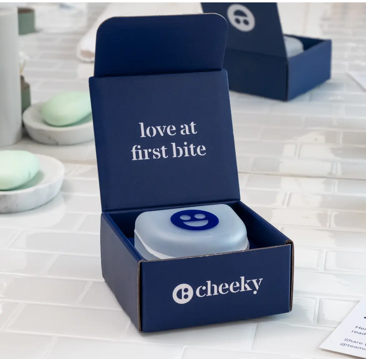Blue box with a product inside, featuring the text 'love at first bite' and 'B cheeky' logo.