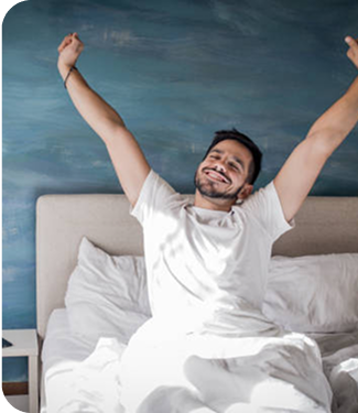 Man in white pajamas sitting on a bed with arms raised against a blue sky background