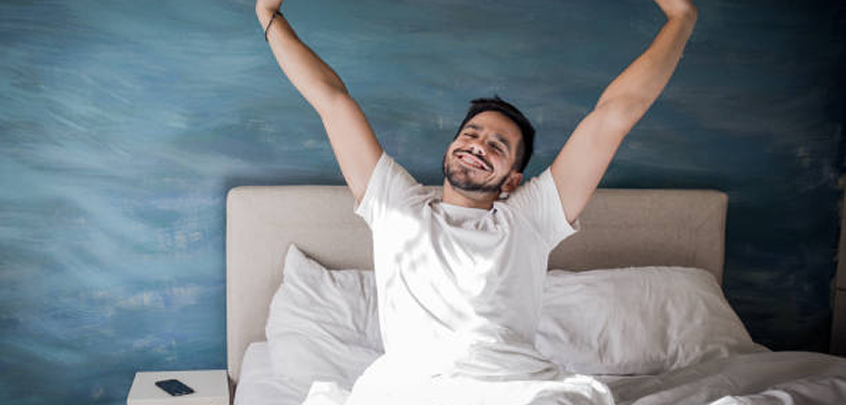 Man stretching in bed with a blue wall in the background