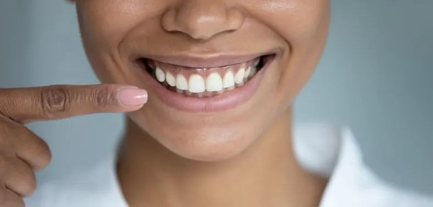 Person pointing to their white teeth with a blurred background