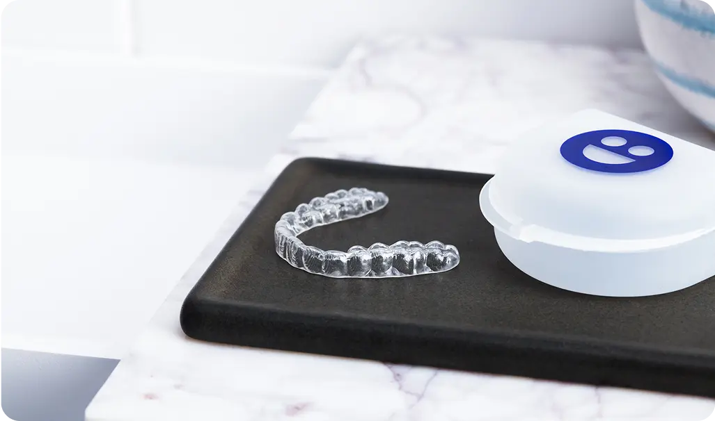 Clear dental aligner and white case on a black tray with a white background
