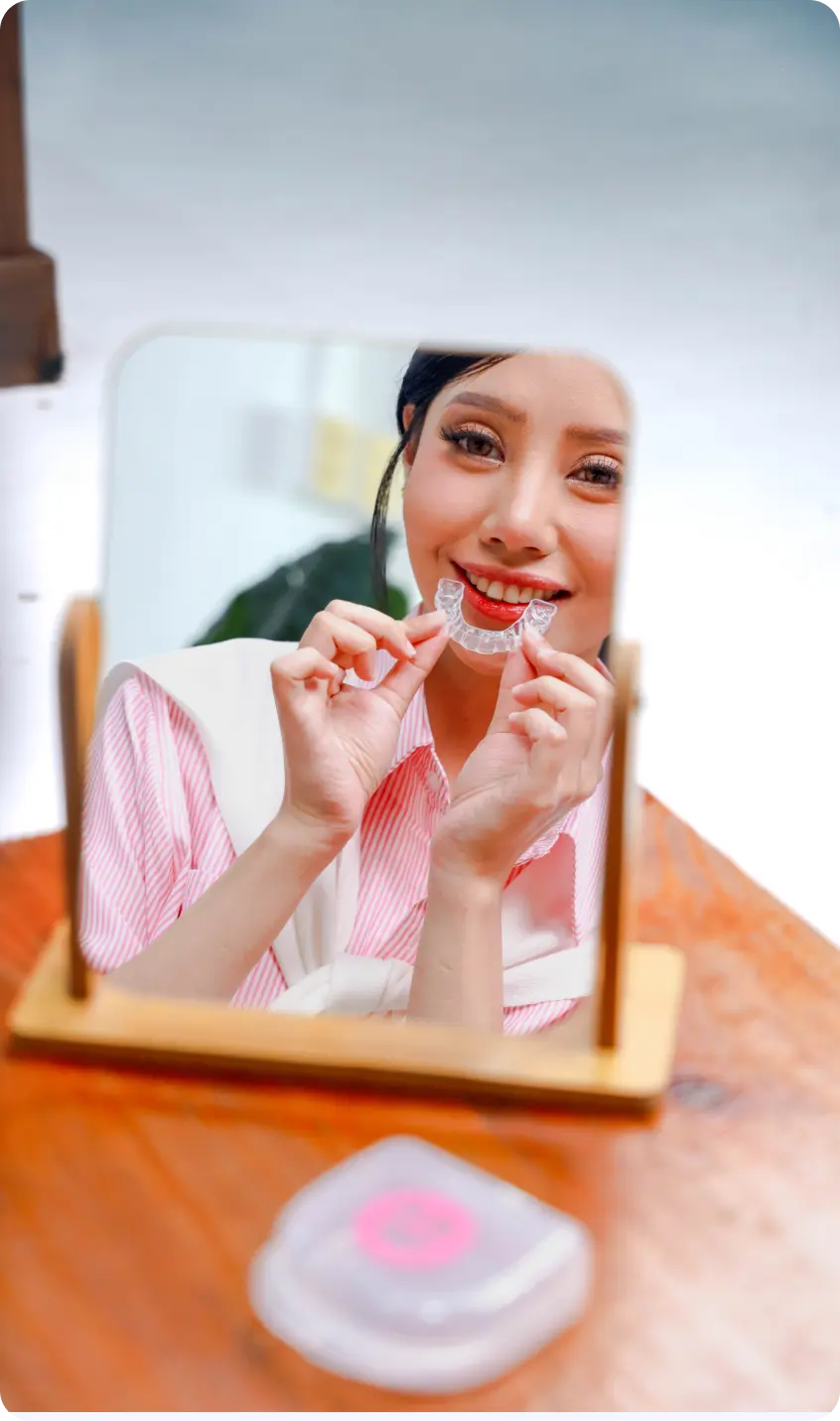 Woman holding a clear dental aligner in front of a mirror.