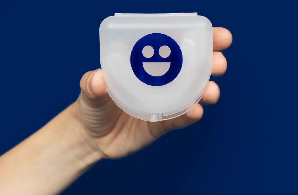 Clear plastic case with smiley face logo held by a hand against a blue background